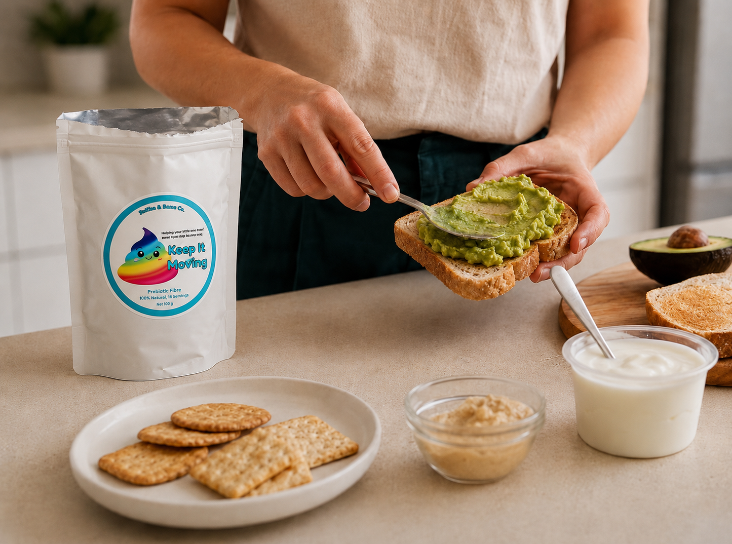 A person spreads avocado toast on a slice of bread while standing at a kitchen counter. A stand-up pouch labelled Keep It Moving Prebiotic Fibre and other food items, including crackers, a small bowl of spread, and a cup of yogurt, are arranged on the counter.